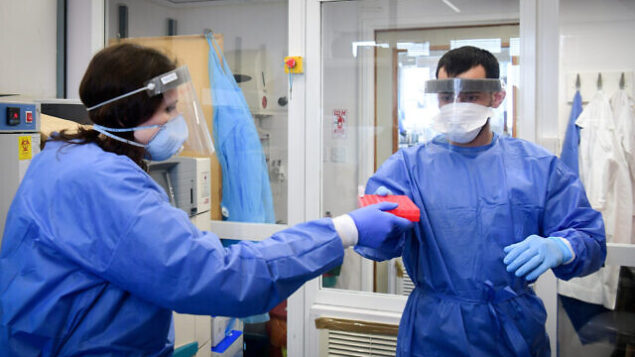 Medical team members at the Barzilay hospital, in the southern Israeli city of Ashkelon, wear protective gear, as they handle a Coronavirus test sample on March 29, 2020. Photo by Flash90 *** Local Caption *** ÷åøåðä
åéøåñ
îâéôä

öååú øôåàé
äöìä
áãé÷åú
ðùàéí
àù÷ìåï
áøæéìàé
