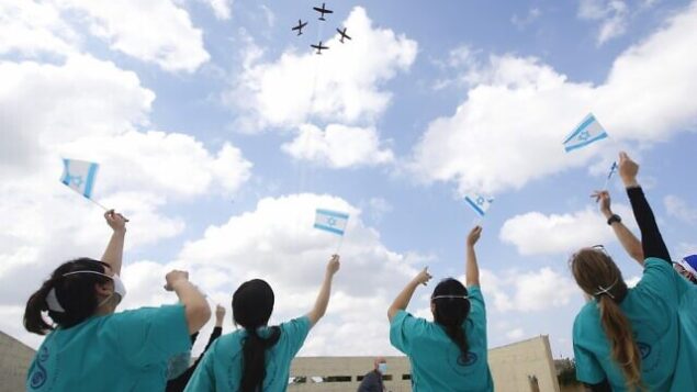 Israeli medical team of Sheba Medical Center at Tel HaShomer, wave national flags as the Israeli Air Force (IAF) fly over the hospital during Israel's Independence day (Yom Ha'atzmaut) celebrations amid the COVID-19 pandemic, in Ramat Gan on April 29, 2020. - Israel celebrates its 72nd anniversary of the declaration of independence in 1948. The annual aviation performance over Israeli beaches was cancelled and made into a solidarity flyover Israeli hospitals during a national closure due to the coronavirus disease (COVID-19) pandemic. (Photo by JACK GUEZ / AFP)