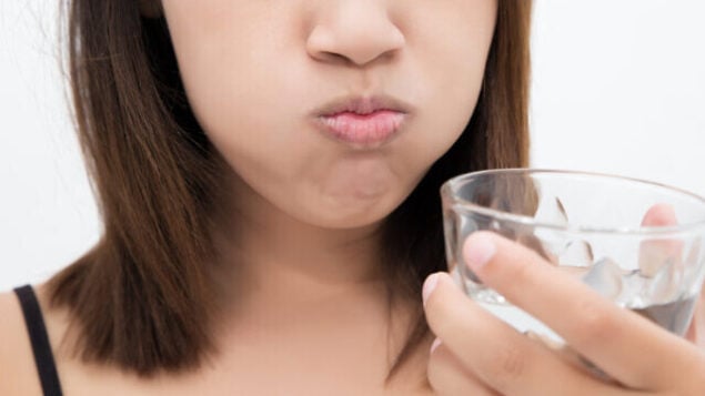 Healthy happy woman rinsing and gargling while using mouthwash from a glass, During daily oral hygiene routine, Portrait with bare shoulders, Dental Health Concepts