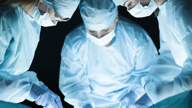 Medical team performing operation. Group of surgeon at work in operating theatre toned in blue