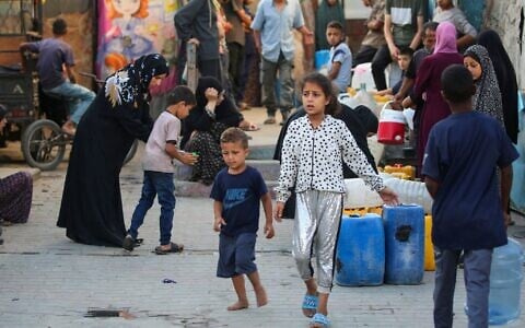 شرح عکس: فلسطینیان در اردوگاه موقت آوارگان، حیاط مدرسهٔ دخترانهٔ ابو حلوی UNRWA، اردوگاه پناهندگی بوریج، مرکز نوار غزه، ۱۷ ژوئیهٔ ۲۰۲۵، که روز پیش مورد اصابت حملهٔ هوایی اسرائیل قرار گرفت، کنار دبه های خود صف کشیده و منتظر تانکر توزیع آب ایستاده اند. (Eyad BABA / AFP)