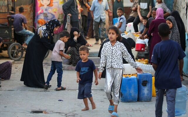 شرح عکس: فلسطینیان در اردوگاه موقت آوارگان، حیاط مدرسهٔ دخترانهٔ ابو حلوی UNRWA، اردوگاه پناهندگی بوریج، مرکز نوار غزه، ۱۷ ژوئیهٔ ۲۰۲۵، که روز پیش مورد اصابت حملهٔ هوایی اسرائیل قرار گرفت، کنار دبه های خود صف کشیده و منتظر تانکر توزیع آب ایستاده اند. (Eyad BABA / AFP)