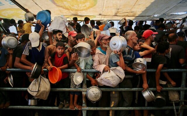 شرح عکس: فلسطینیان مقابل آشپزخانهٔ خیریه در مواسی برای دریافت غذای گرم صف کشیده اند؛ خان یونس، جنوب نوار غزه، ۲۲ ژوئیهٔ ۲۰۲۵. (Photo by AFP)