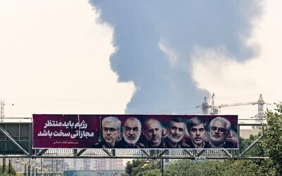 شرح عکس: تزئینی -  تصاویری از فرماندهان نظامی و دانشمندان هسته ای ایران که در حملهٔ ۱۳ ژوئن اسرائیل کشته شدند، بالای خیابان به نمایش گذاشته شده، و بر فراز پالایشگاه نفت در جنوب تهران، که در ۱۵ ژوئن ۲۰۲۵ بمباران شد، دودی غلیظ بهوا خاسته است. (Atta Kenare/AFP)