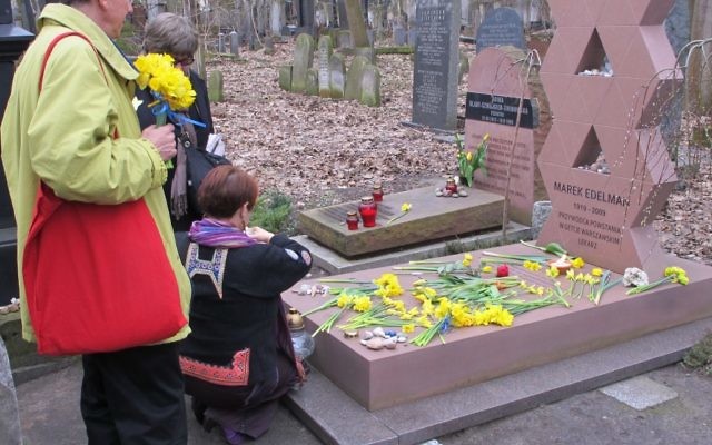 Des visiteurs placent des jonquilles sur la tombe de Marek Edelman, commandant du soulèvement du ghetto de Varsovie, dans le cimetière juif de Varsovie. (Ruth Ellen Gruber / JTA)