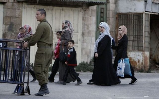 Des femmes arabes passent à côté d'un soldat israélien en patrouille dans la ville divisée de Hébron en Cisjordanie. (Crédit : Miriam Alster/Flash90)