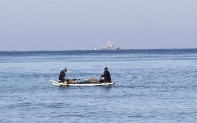 Des pêcheurs palestiniens assis dans leur barque à proximité du rivage de Rafah, au sud de Gaza ; un bateau de police israélien apparaît au loin, le 26 mars 2014. (Crédit : Said Khatib/AFP)
