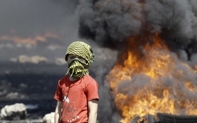Un garçon palestinien masqué à côté de pneus en feu (Crédit : Jaafar Ashtiyeh/AFP) Un garçon palestinien masqué à côté de pneus en feu (Crédit : Jaafar Ashtiyeh/AFP)