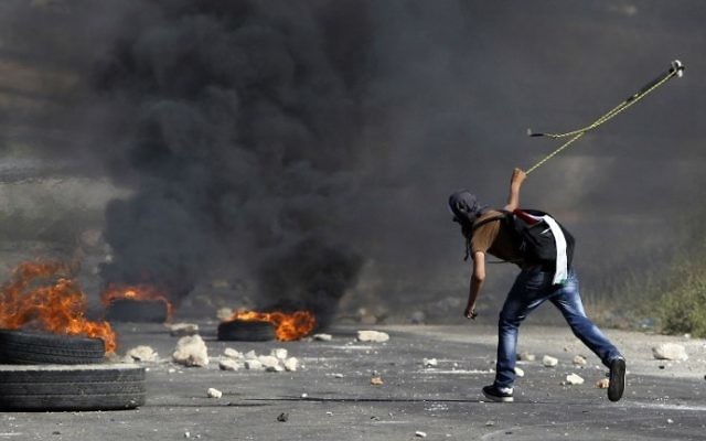 Un Palestinien qui lance des pierres contre les forces israéliennes près de la prison d'Ofer (Crédit : AFP/Abbas Momani) Un Palestinien qui lance des pierres contre les forces israéliennes près de la prison d'Ofer (Crédit : AFP/Abbas Momani)
