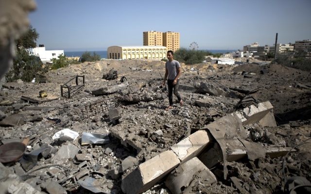 Un Palestinien marchant sur des ruines après un raid israélien (Crédit : AFP/MOHAMMED ABED) Un Palestinien marchant sur des ruines après un raid israélien (Crédit : AFP/MOHAMMED ABED)