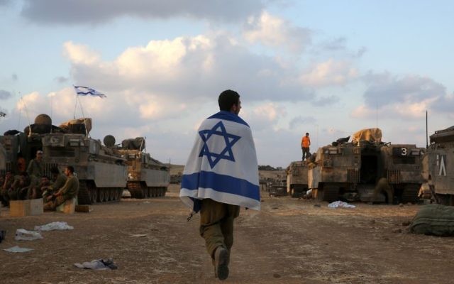 Un soldat israélien porte le drapeau israélien à Gaza - 19 juillet 2014 (Crédit : Nati Shohat/Flash90) Un soldat israélien porte le drapeau israélien à Gaza - 19 juillet 2014 (Crédit : Nati Shohat/Flash90)