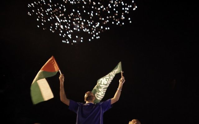Des Palestiniens tiennent un drapeau palestinien et un drapeau du Hamas alors que des feux d'artifice illuminent le ciel le 26 août, 2014 à Jérusalem-Est (Crédit : AFP PHOTO / AHMAD GHARABLI Des Palestiniens tiennent un drapeau palestinien et un drapeau du Hamas alors que des feux d'artifice illuminent le ciel le 26 août, 2014 à Jérusalem-Est (Crédit : AFP PHOTO / AHMAD GHARABLI