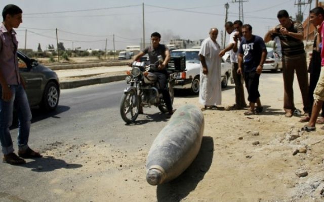 Des Palestiniens devant une munition non explosée sur une rue à Deir El-Balah dans la bande de Gaza - 1 août 2014 (Crédit : Mostafa Ashqar / FLASH90)