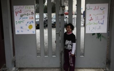 Une enfant arabe devant l'entrée d'une école où l'on peut lire des mots de haine (Crédit : Kobi Gideon/Flash90)