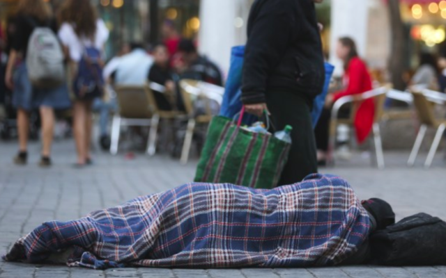 Des gens passent à côté d'un sans-abri qui dort dans la rue, près des cafés du centre de Jérusalem. Le 10 novembre 2013. (Nati Shohat/FLASH90) Des gens passent à côté d'un sans-abri qui dort dans la rue, près des cafés du centre de Jérusalem. Le 10 novembre 2013. (Nati Shohat/FLASH90)