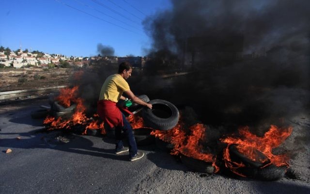 Un jeune Palestinien du camp de réfugiés Jilazoun brûle des pneus sur la route menant à Bet El, près de Ramallah lors d'affrontements avec des soldats israéliens 24 octobre 2014 (Crédit : STR / Flash90)