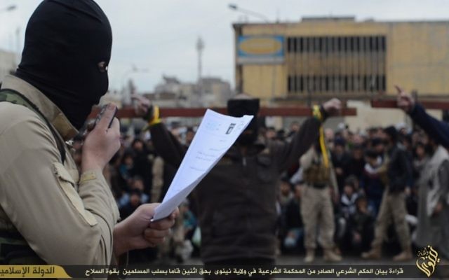 Un combattant de l'Etat islamique lisant les charges contre deux personnes crucifiées (en arrière plan) (Crédit : Capture d'écran) Un combattant de l'Etat islamique lisant les charges contre deux personnes crucifiées (en arrière plan) (Crédit : Capture d'écran)