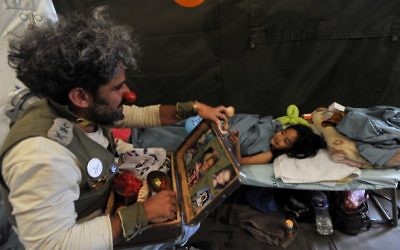 Un clown 'médical' israélien divertit une victime du tremblement de terre du Népal lors d'une visite dans un camp de l'armée de fortune à Katmandou le 6 mai 2015. Le tremblement de terre de magnitude 7,8 qui a frappé la nation himalayenne le 25 avril 2015 et a eu un impact dévastateur sur l'économie du Népal où le tourisme a attiré près de 800 000 visiteurs étrangers en 2013 (Crédit : AFP PHOTO / PRAKASH MATHEMA)