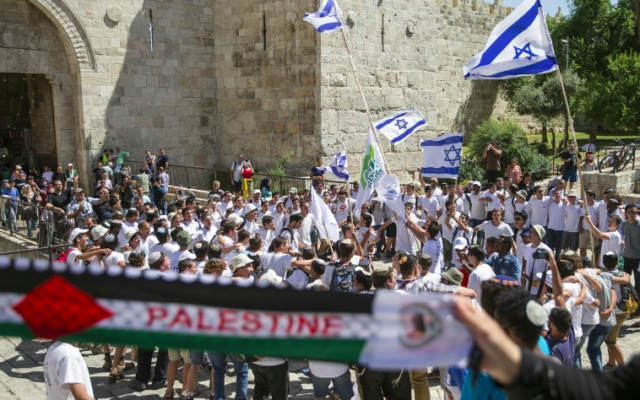 Des femmes palestiniennes brandissant une écharpe en faveur  de la Palestine alors que de jeunes israéliens brandissent leur drapeau national dans la "marche des drapeaux" passant devant la porte de Damas, dans la Vieille Ville de Jérusalem lors des célébrations de Yom Yeroushalayim, le 17 mai 2015. (Crédit photo: AFP / Jack Guez)
