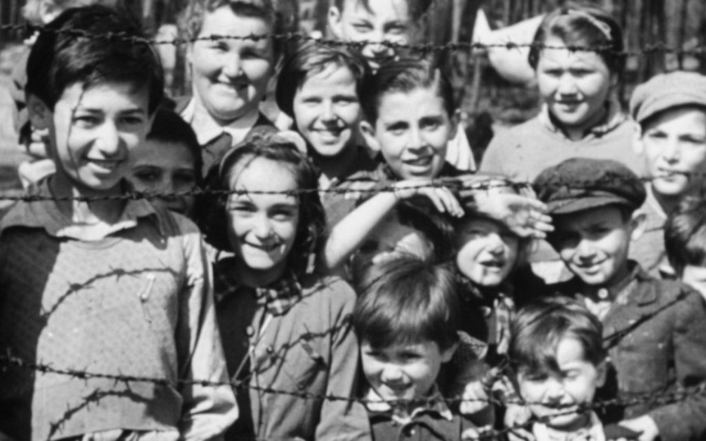 Une photo extraite de "L'enquête factuelle sur les camps de concentration allemands " montrant des enfants souriants à travers les barbelés à l'arrivée les troupes alliées, avril 1945. (Imperial War Museum)