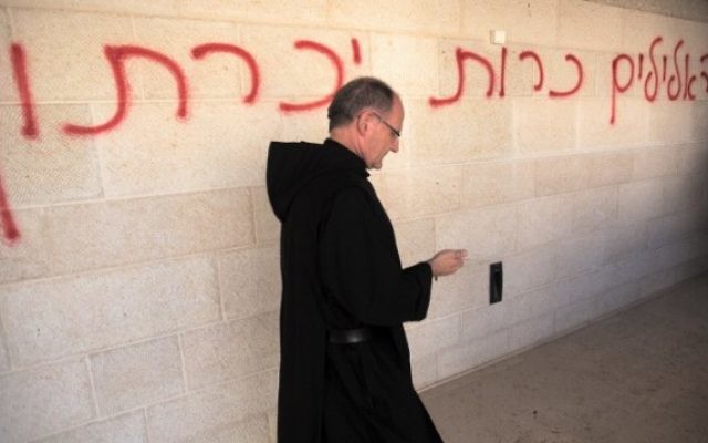 Un prêtre passe à côté d’un graffiti en hébreu, disant « les fausses idoles seront éliminées », pendant qu’il inspecte les dommages à l’église de la Multiplication de Tabgha, sur les rives du lac de Tibériade dans le nord d’Israël, le 18 juin 2015. (Crédits : AFP / Menahem Kahana) Un prêtre passe à côté d’un graffiti en hébreu, disant « les fausses idoles seront éliminées », pendant qu’il inspecte les dommages à l’église de la Multiplication de Tabgha, sur les rives du lac de Tibériade dans le nord d’Israël, le 18 juin 2015. (Crédits : AFP / Menahem Kahana)