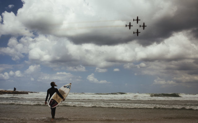 Un surfeur regarde le spectacle des forces aériennes israéliennes sur le  Jour de l'Indépendance sur une plage de Tel Aviv le 23 avril 2015 (Crédit : Matanya Tausig / Flash90)