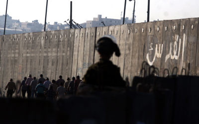 Un soldat de Tsahal observe des Palestiniens qui traversent le poste de contrôle de Qalandiya près de la ville de Ramallah en Cisjordanie (Crédit : Issam Rimawi / Flash90)
