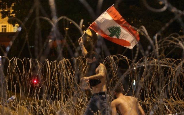 Un Libanais agite un drapeau national alors qu'il tente de franchir les barbelés séparant les manifestants du palais gouvernemental lors d'un rassemblement de masse contre une classe politique considérée comme corrompue et incapable de fournir les services de base le 29 août 2015 sur la place des Martyrs de Beyrouth. (AFP PHOTO / STR)