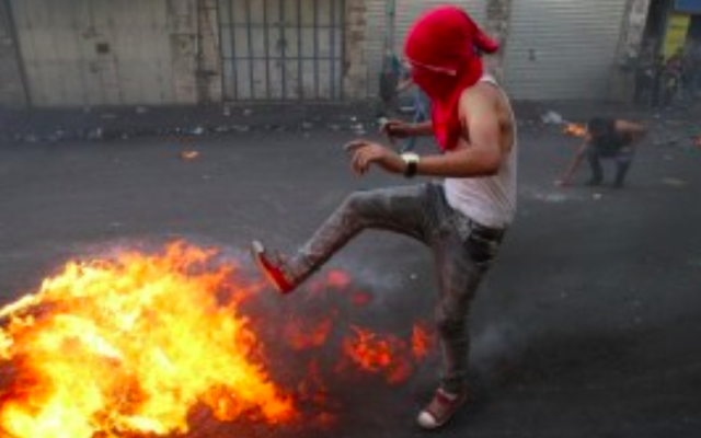 Un jeune Palestinien lance un pneu en train de brûler lors d'affrontements avec les forces de sécurité israéliennes dans la ville d'Hébron en Cisjordanie, le 4 octobre, 2015. (Crédit : AFP / HAZEM BADER) Un jeune Palestinien lance un pneu en train de brûler lors d'affrontements avec les forces de sécurité israéliennes dans la ville d'Hébron en Cisjordanie, le 4 octobre, 2015. (Crédit : AFP / HAZEM BADER)