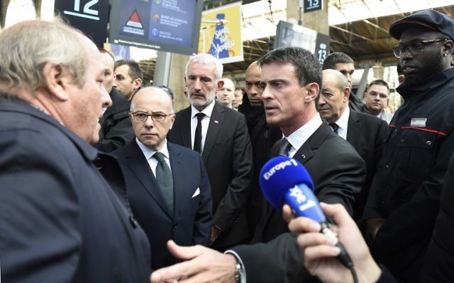 Un homme (g), qui est à la recherche de sa fille, qui avait été au Bataclan dans la nuit des attaques de Paris le 13 novembre, parle avec le Premier ministre français Manuel Valls (3e D), le ministre de la Défense français Jean-Yves Le Drian (2e D), le président de la SNCF Guillaume Pepy (C) et le ministre de l'Intérieur français Bernard Cazeneuve (2e g) à la gare du Nord à Paris, le 15 Novembre 2015. (Crédit : AFP PHOTO / ERIC FEFERBERG)