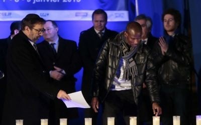 Lassana Bathily allume des bougies le 9 Janvier, 2016 près de l'Hyper Cacher,  lors d'une cérémonie organisée pour rendre hommage aux victimes de l'attentat contre le supermarché le 9 Janvier 2015 (Crédit : AFP / JACQUES DEMARTHON)