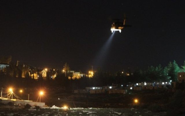 Le village palestinien de Dahriya, avec un hélicoptère de l'armée israélienne volant au-dessus de l'implantation d'Otniel, au sud de la Cisjordanie, alors que les forces de l'ordre recherchent un Palestinien suspecté d'avoir poignardé et tué Dafna Meir chez elle, le 17 janvier 2016. (Crédit : AFP/Hazem Bader)