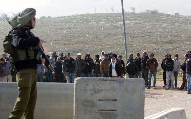 Un soldat israélien de garde pendant que les travailleurs palestiniens sont transportés en-dehors de l'implantation de Tekoa, au sud de Jérusalem, à la suite d'une attaque terroriste dans la communauté le 18 janvier 2016. (Crédit : AFP / MENAHEM KAHANA) Un soldat israélien de garde pendant que les travailleurs palestiniens sont transportés en-dehors de l'implantation de Tekoa, au sud de Jérusalem, à la suite d'une attaque terroriste dans la communauté le 18 janvier 2016. (Crédit : AFP / MENAHEM KAHANA)