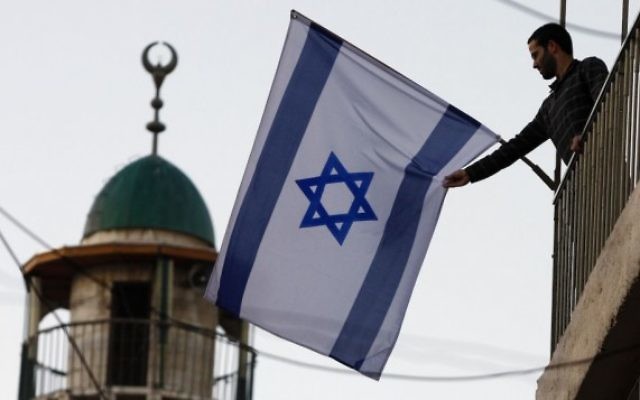 Un Israélien juif brandissant un drapeau israélien près de la Vieille Ville de Jérusalem, qui a vu un afflux de résidents juifs dans des quartiers majoritairement arabes. (Crédit : Abir Sultan/Flash 90)