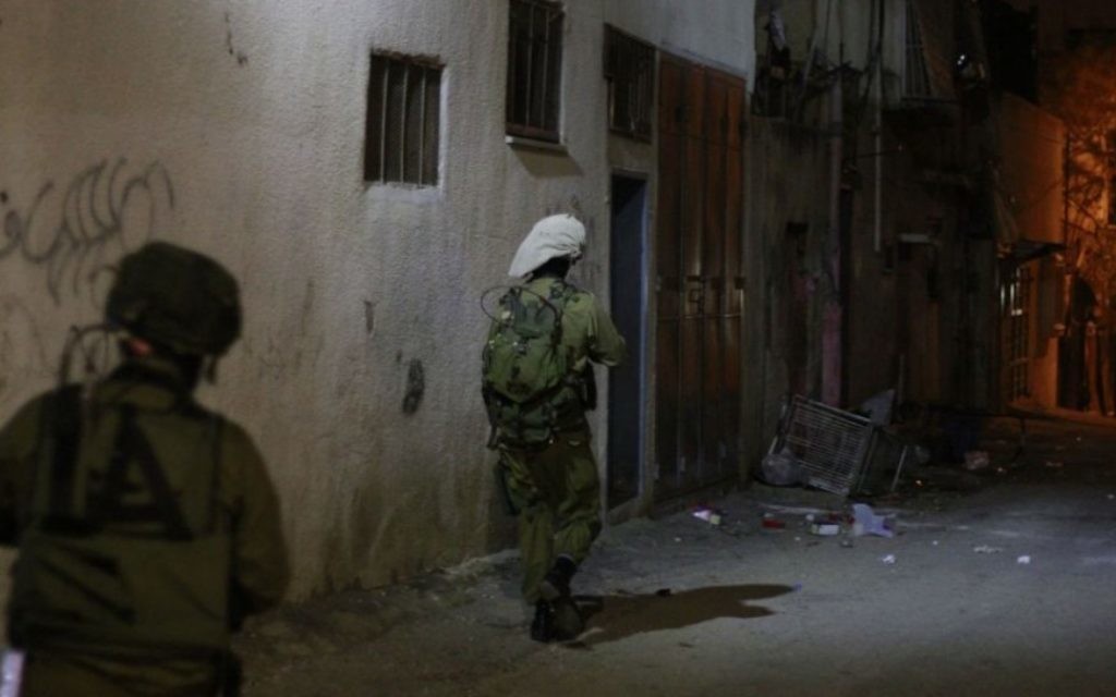 Des soldats de l’armée israélienne avancent vers la maison de deux adolescents palestiniens suspectés d’avoir pris part à de violentes manifestations à Qalqilya. Un représentant arabophone du coordinateur des activités gouvernementales dans les Territoires accompagne le bataillon pour faciliter la conversation entre les soldats et les familles des accusés, le 14 janvier 2016. (Crédit : Judah Ari Gross/Times of Israel)
