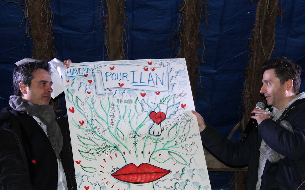 Laurent Barilan-Pariente, président du collectif Haverim, et Philippe Elie Kassabi, artiste, qui tiennent une œuvre signée par les intervenants de la commémoration du 11 février et qui sera prochainement mise aux enchères (Crédit : Times of Israël Staff/Glenn Cloarec)