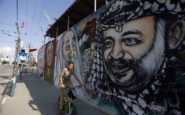 Un garçon palestinien sur son vélo passant devant une fresque de graffitis représentant (de gauche à droite) le fondateur du Front Populaire pour la Libération de la Palestine (FPLP) Georges Habache, le chef spirituel du Hamas, le cheikh Ahmed Yassine et le dirigeant palestinien défunt Yasser Arafat, le 21 novembre 2014 dans la ville de Gaza. (Crédit : AFP / MOHAMMED ABED)