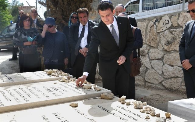 Le Premier ministre français Manuel Valls (C) visite les tombes de Jonathan, Arie et Gabriel Sandler, qui ont été tués en mars 2012 dans une attaque terroriste contre une école juive dans la ville française de Toulouse, au cimetière de Givat Shaul à Jérusalem le 23 mai 2016. (Crédit : Menahem Kahana/AFP)