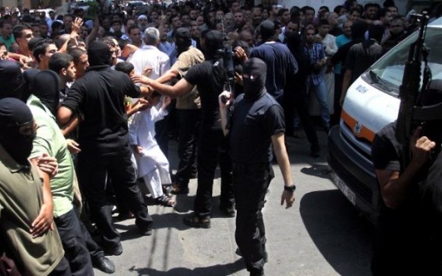 Un Palestinien armé et masqué repousse une foule de croyants devant la mosquée de Gaza Ville après la prière du vendredi, avant l'exécution de 18 hommes qui auraient collaboré avec Israël, le 22 août 2O14. (Crédit : AFP) Un Palestinien armé et masqué repousse une foule de croyants devant la mosquée de Gaza Ville après la prière du vendredi, avant l'exécution de 18 hommes qui auraient collaboré avec Israël, le 22 août 2O14. (Crédit : AFP)