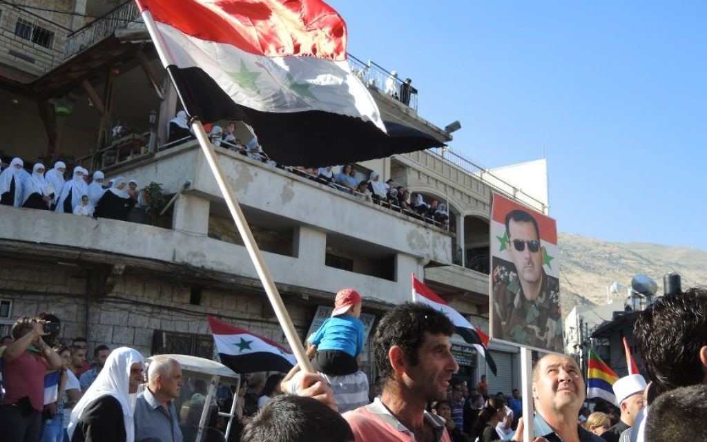 Un homme porte un drapeau syrien et un poster du présidet Bashar Al Assad au cours d'une manifestation pro armée syrienne, à Majdal Shams, lundi (Crédit : Melanie Lidman/Times of Israel)
