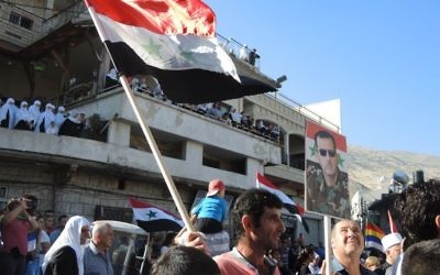 Un homme porte un drapeau syrien et un poster du présidet Bashar Al Assad au cours d'une manifestation pro armée syrienne, à Majdal Shams, lundi (Crédit : Melanie Lidman/Times of Israel) Un homme porte un drapeau syrien et un poster du présidet Bashar Al Assad au cours d'une manifestation pro armée syrienne, à Majdal Shams, lundi (Crédit : Melanie Lidman/Times of Israel)