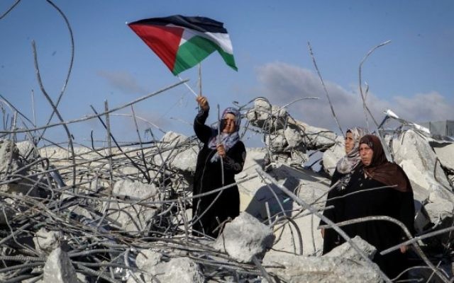 La mère du terroriste palestinien Morad Bader Abdullah Adais brandit un drapeau palestinien en se tenant sur les ruines de leur maison après sa démolition par l'armée israélienne à Yatta, au sud de Hébron, en Cisjordanie, le 11 juin 2016. Adais avait poignardé à mort Dafna Meir, mère de six enfants, en janvier. (Crédit : Wisam Hashlamoun/Flash90)