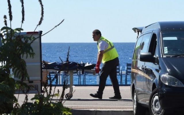 Un médecin légiste évacue un corps, sur la Promenade des Anglais, sur la Côte d'Azur, dans la ville de Nice, le 15 juillet 2016, après qu'un homme armé ait précipité un camion dans la foule venue célébrer la fête nationale, tuant au moins 84 personnes (Crédit : AFP Photo/Boris Horvat)