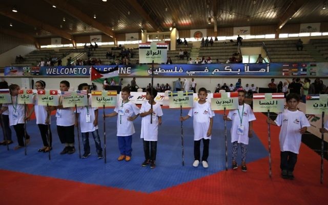 Des enfants portent des bannières portant les noms et les drapeaux des pays participant au championnat international de taekwondo à Birzeit, à Ramallah, en Cisjordanie, le 18 juillet 2016. (Crédit : AFP/Abbas Momani)