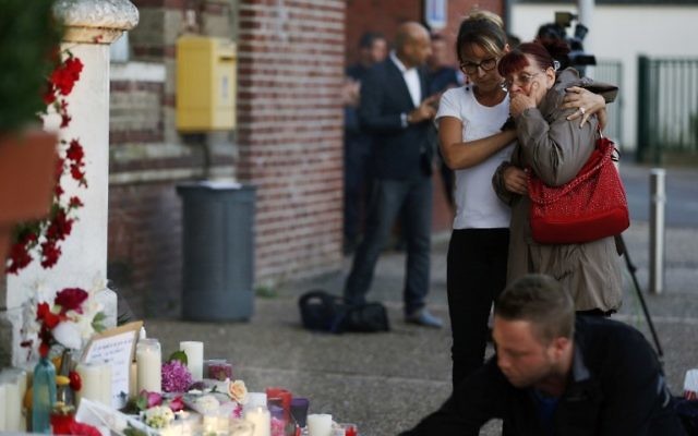Deux femmes près des fleurs et des messages affichés en face de la mairie de la ville normande de Saint-Etienne du Rouvray, en hommage au prêtre tué dans l'église de la ville, une attaque revendiquée par le groupe djihadiste de l'Etat islamique, le 26 juillet 2016. (Crédit : AFP/ CHARLY TRIBALLEAU)