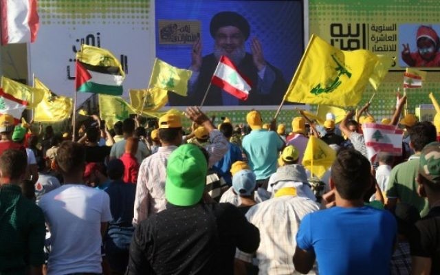 De jeunes hommes agitent des drapeaux libanais ou du groupe terroriste chiite du Hezbollah pendant un discours de Hassan Nasrallah, chef de l'organisation, commémorant les dix ans de la deuxième guerre du Liban, le 13 août 2016. (Crédit : Mahmoud Zayyat/AFP) De jeunes hommes agitent des drapeaux libanais ou du groupe terroriste chiite du Hezbollah pendant un discours de Hassan Nasrallah, chef de l'organisation, commémorant les dix ans de la deuxième guerre du Liban, le 13 août 2016. (Crédit : Mahmoud Zayyat/AFP)