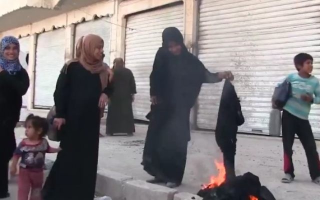 Une Syrienne brûle une burqa pour célébrer la libération de la ville de Manbij du contrôle de l'EI, le 13 août 2016. (Crédit : Capture d'écran / K24) Une Syrienne brûle une burqa pour célébrer la libération de la ville de Manbij du contrôle de l'EI, le 13 août 2016. (Crédit : Capture d'écran / K24)