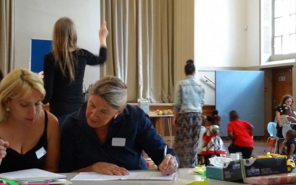 Des bénévoles aident les réfugiés à remplir des formulaires, pendant que les enfants jouent, au centre d'accueil de la West London Synagogue Des bénévoles aident les réfugiés à remplir des formulaires, pendant que les enfants jouent, au centre d'accueil de la West London Synagogue