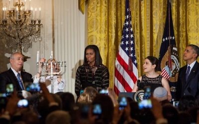 Mika Almog, petite-fille de l'ancien président israélien Shimon Peres, allume la hanoukkiah pendant que madame le rabbin Rachel Isaacs récite les bénédictions dans l'East Room de la Maison Blanche le 14 décembre 2016 à Washington, DC, avec Chemi Peres, le président Barack Obama et la Première dame Michelle Obama. (Crédit : AFP/ ZACH GIBSON)