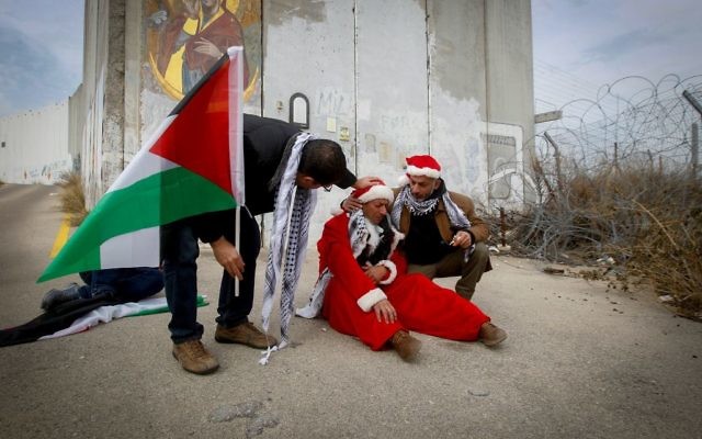 Des manifestants palestiniens déguisés en Pères Noël durant une manifestation devant le mur de sécurité à Bethléem, le 23 décembre 2016. (Crédit : Wisam Hashlamoun/FLASH90) Des manifestants palestiniens déguisés en Pères Noël durant une manifestation devant le mur de sécurité à Bethléem, le 23 décembre 2016. (Crédit : Wisam Hashlamoun/FLASH90)